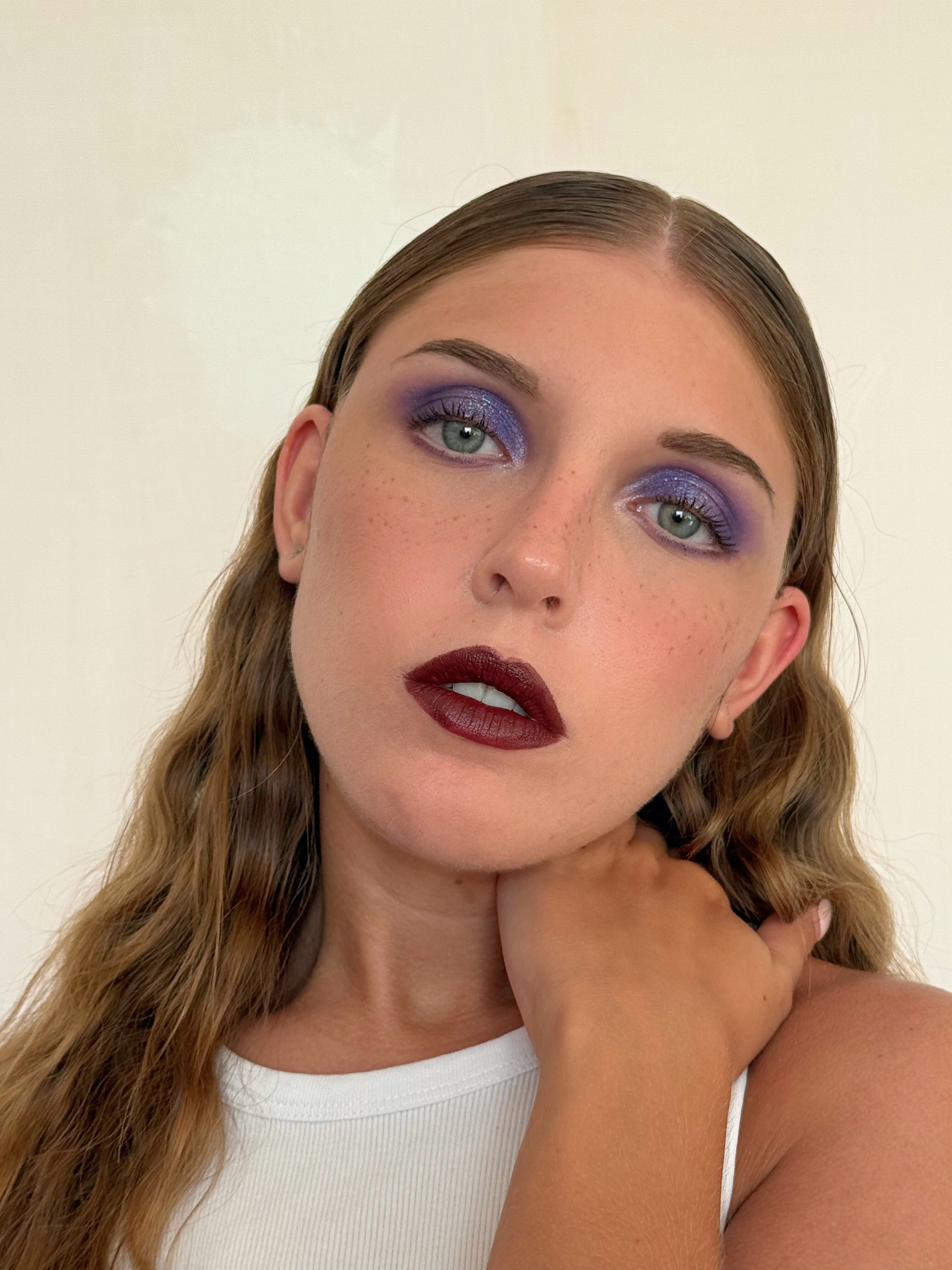 A bold and captivating look with shimmering purple eyeshadow, perfectly blended for a dramatic effect, paired with deep burgundy lips that enhance the intensity of the gaze.